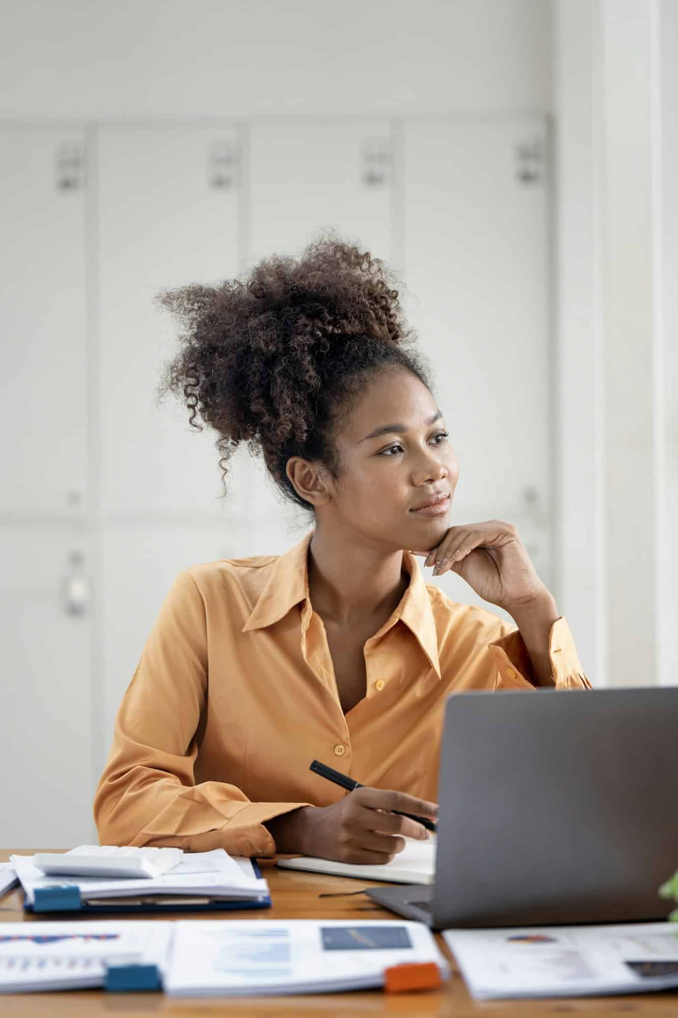 Gelukkige zwarte zakenvrouw zit op kantoor voor haar laptop en denkt na.