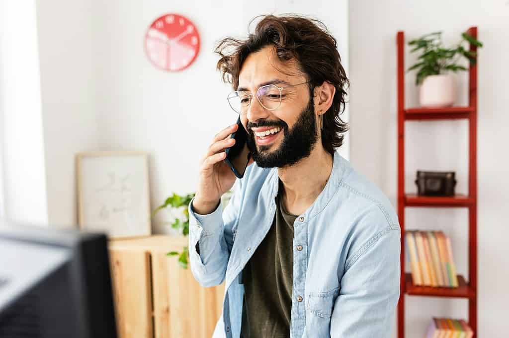 Glimlachende man die aan de telefoon praat terwijl hij thuis aan het werk is.